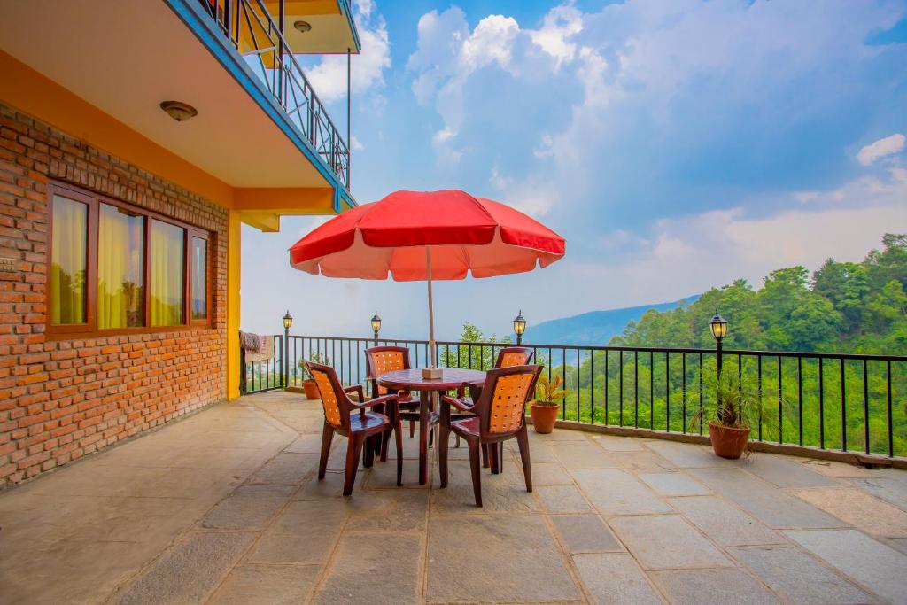 a table and chairs with a red umbrella on a balcony at Sunrise Moon Beam Hotel in Nagarkot