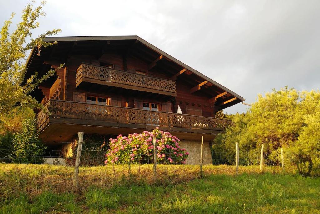 a wooden house with a balcony and pink flowers at Chalet paisible dans la nature avec belle vue sur le lac Léman in Lugrin