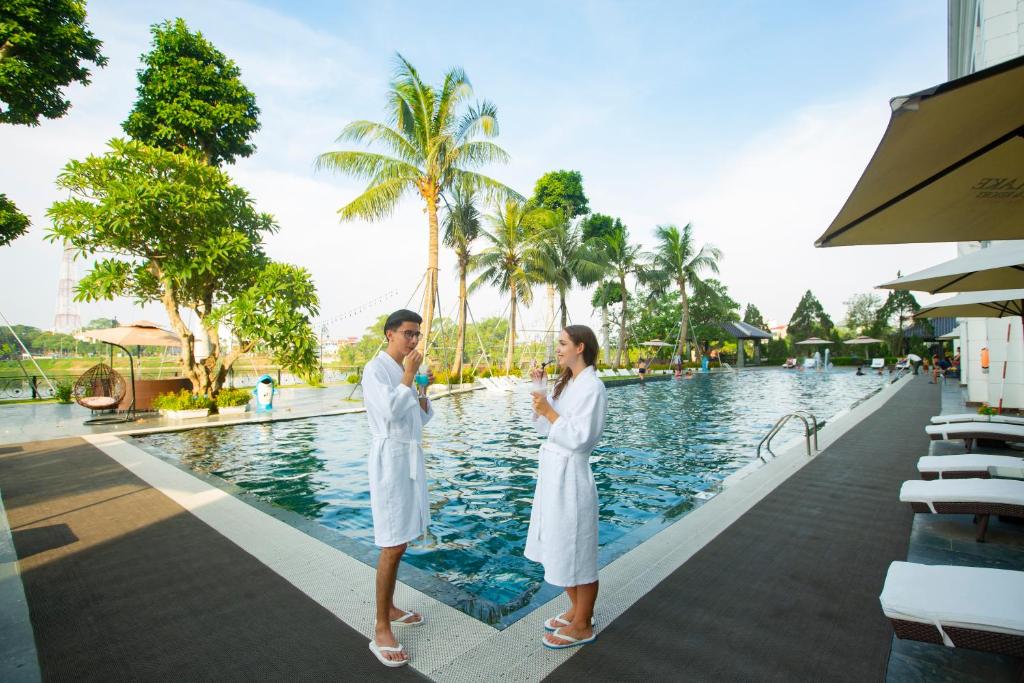 YenにあるWestlake Hotel & Resort Vinh Phucの白いローブを着た2名用のスイミングプールの横に立つ