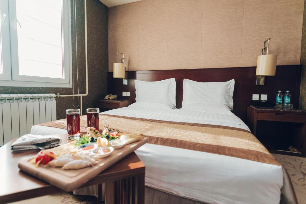a hotel room with a bed and a tray of food at Soluxe Hotel Almaty in Almaty