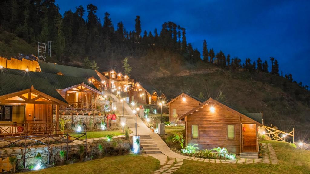 a row of wooden buildings with lights at night at Woodays Resort in Shimla