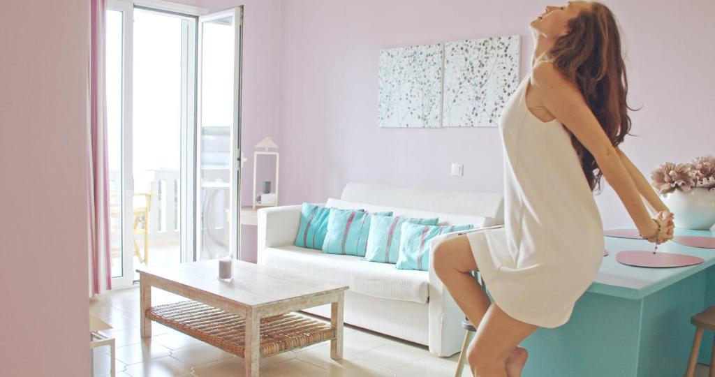 Waterlily Hotel Apartments في كالاثاس: امرأة ترتدي ثوب أبيض تقف على طاولة في غرفة المعيشة