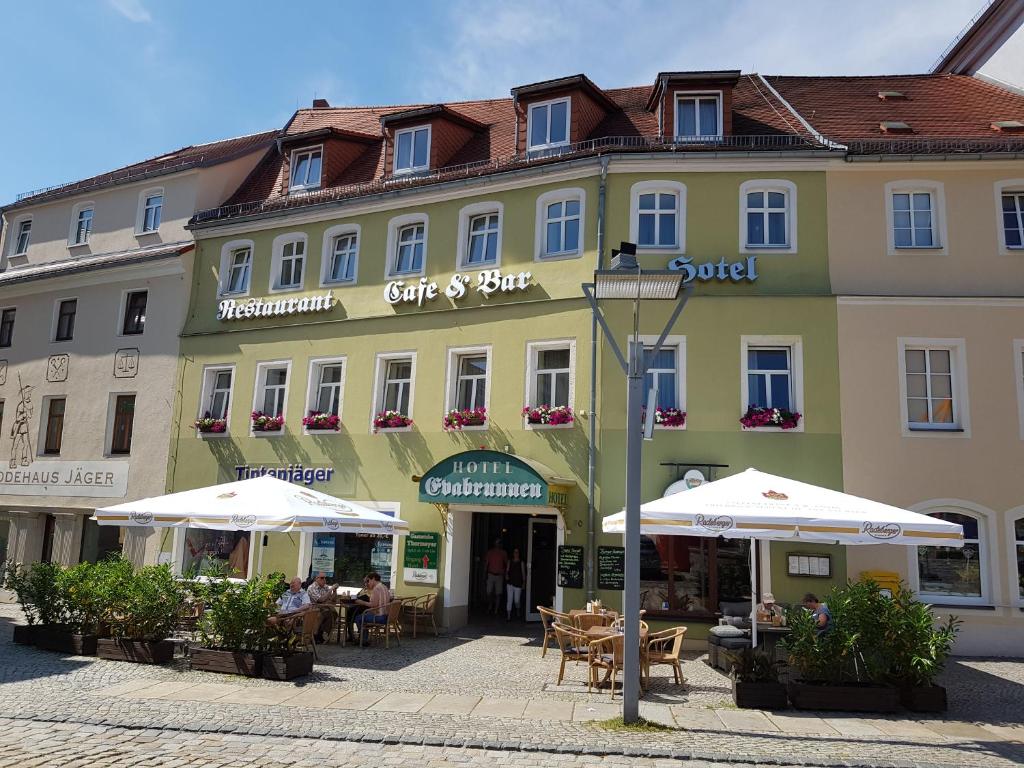 a large yellow building with tables and umbrellas at Hotel Evabrunnen in Bischofswerda