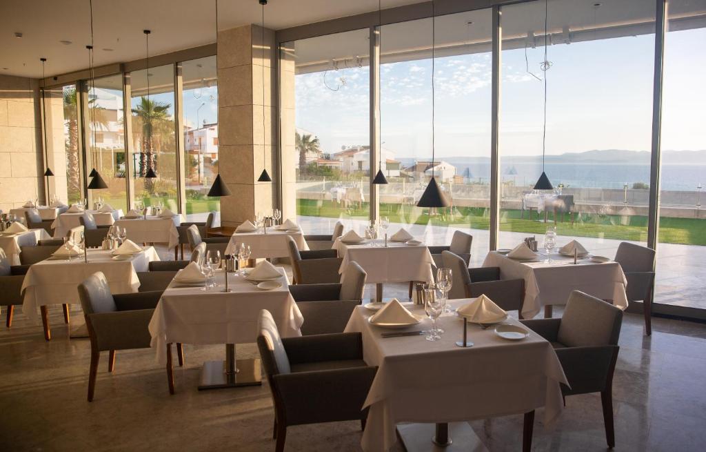 a restaurant with white tables and chairs and large windows at ON'LIVE HOTEL in Çeşme