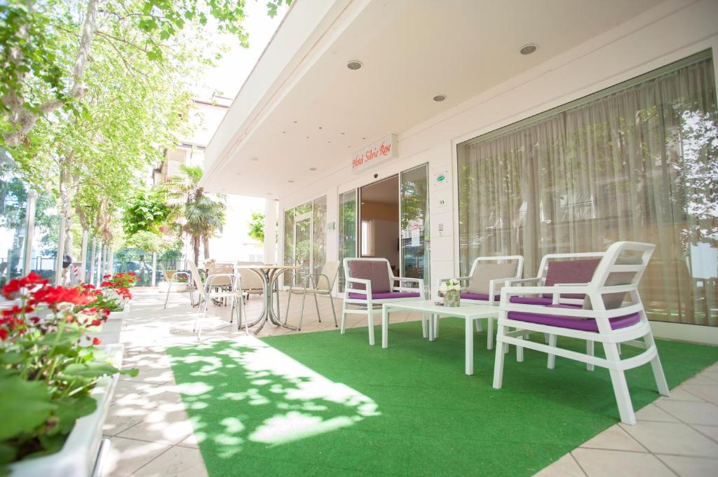 a patio with white chairs and tables and flowers at Villa Silvie Rose in Cesenatico