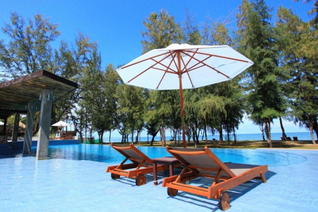 a pool with two chairs and a table with an umbrella at Hansar Casuarina Cha am in Puk Tian