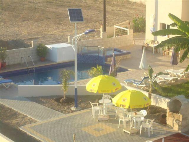 two yellow umbrellas and chairs next to a swimming pool at Marios Apartments in Pervolia