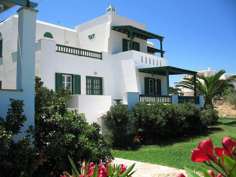 ein weißes Haus mit grünen Rollläden und einem Hof in der Unterkunft HOTEL KAPARI in Agia Anna