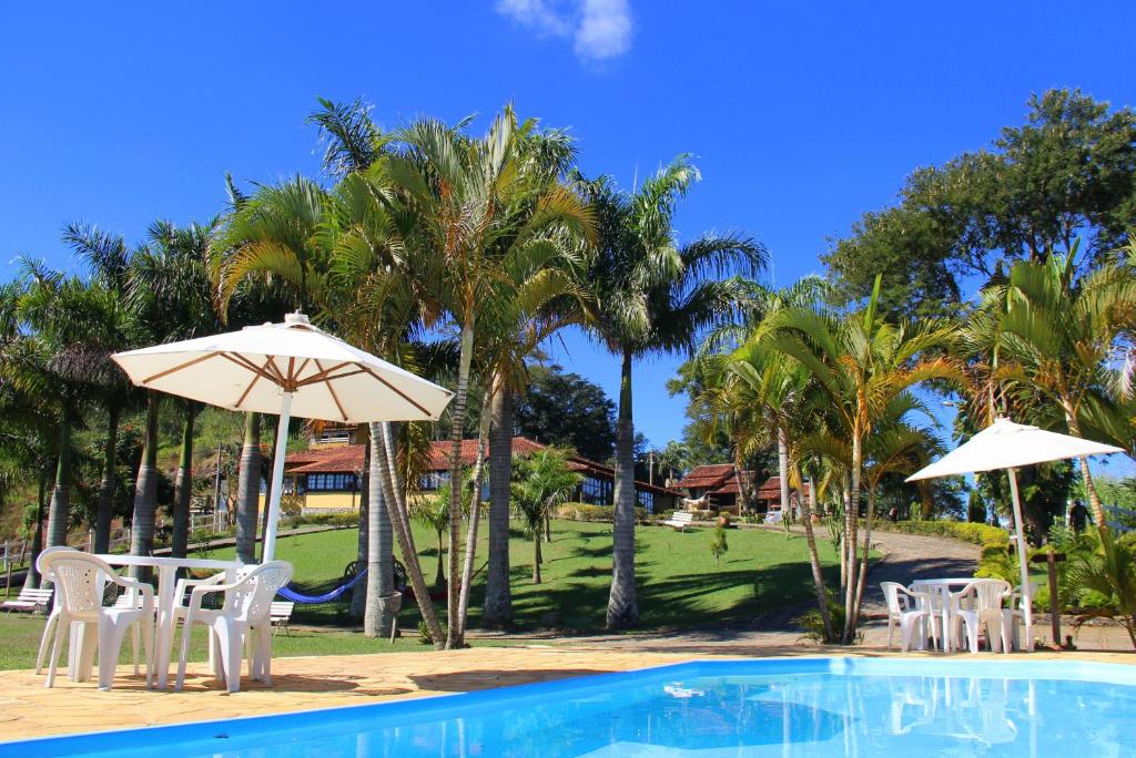 una piscina con sillas y sombrillas blancas y palmeras en Pousada Chapadão, en Ipiabas