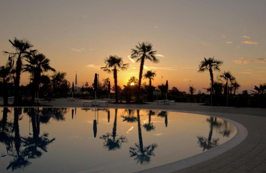 a pool with palm trees and the sunset in the background at Villaggio Laguna Blu in Caorle