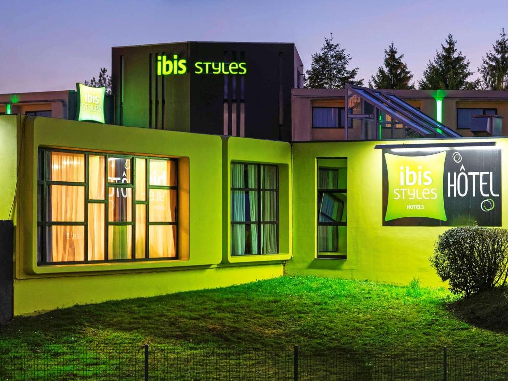 un bâtiment vert avec deux panneaux sur son côté dans l'établissement ibis Styles Chalon sur Saône, à Chalon-sur-Saône