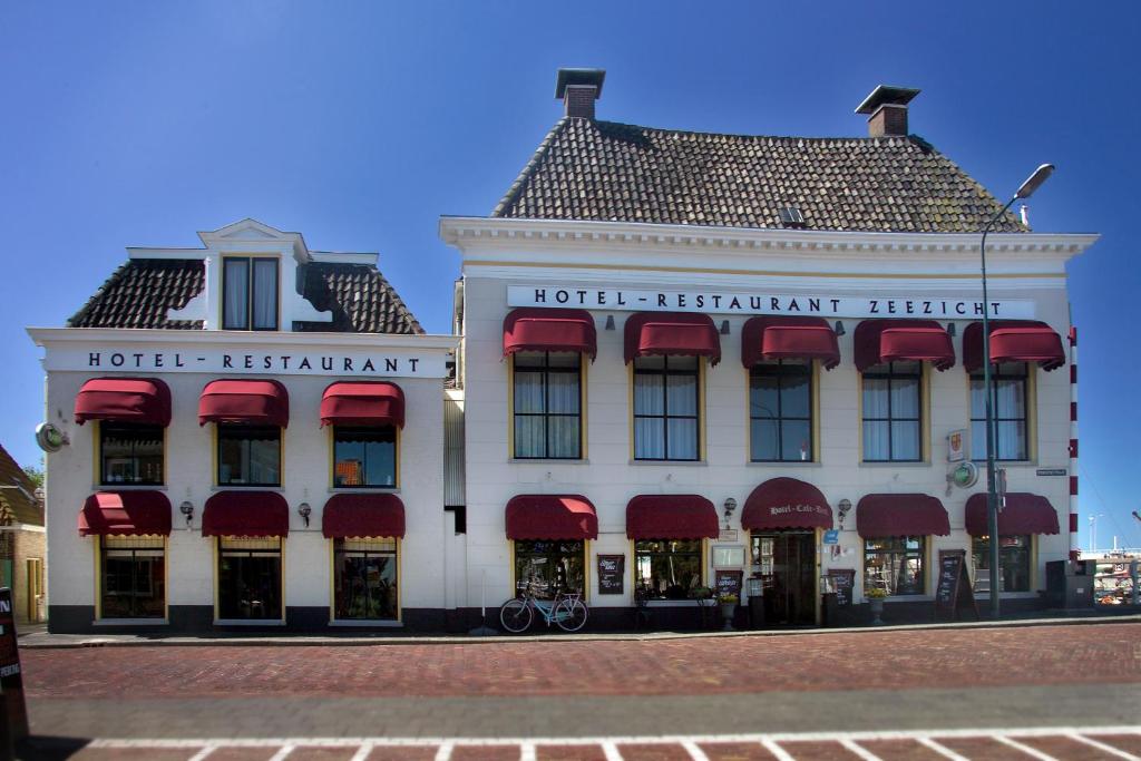 un gran edificio blanco con toldos rojos. en Hotel Zeezicht en Harlingen