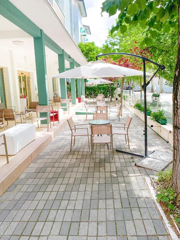 eine Terrasse mit Tischen, Stühlen und einem Sonnenschirm in der Unterkunft Hotel Zamagna in Cesenatico