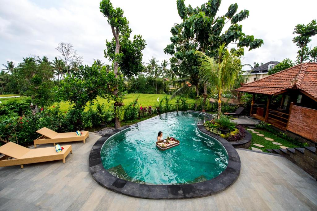 Una piscina en un complejo con dos personas en un barco. en Puri Kobot en Ubud