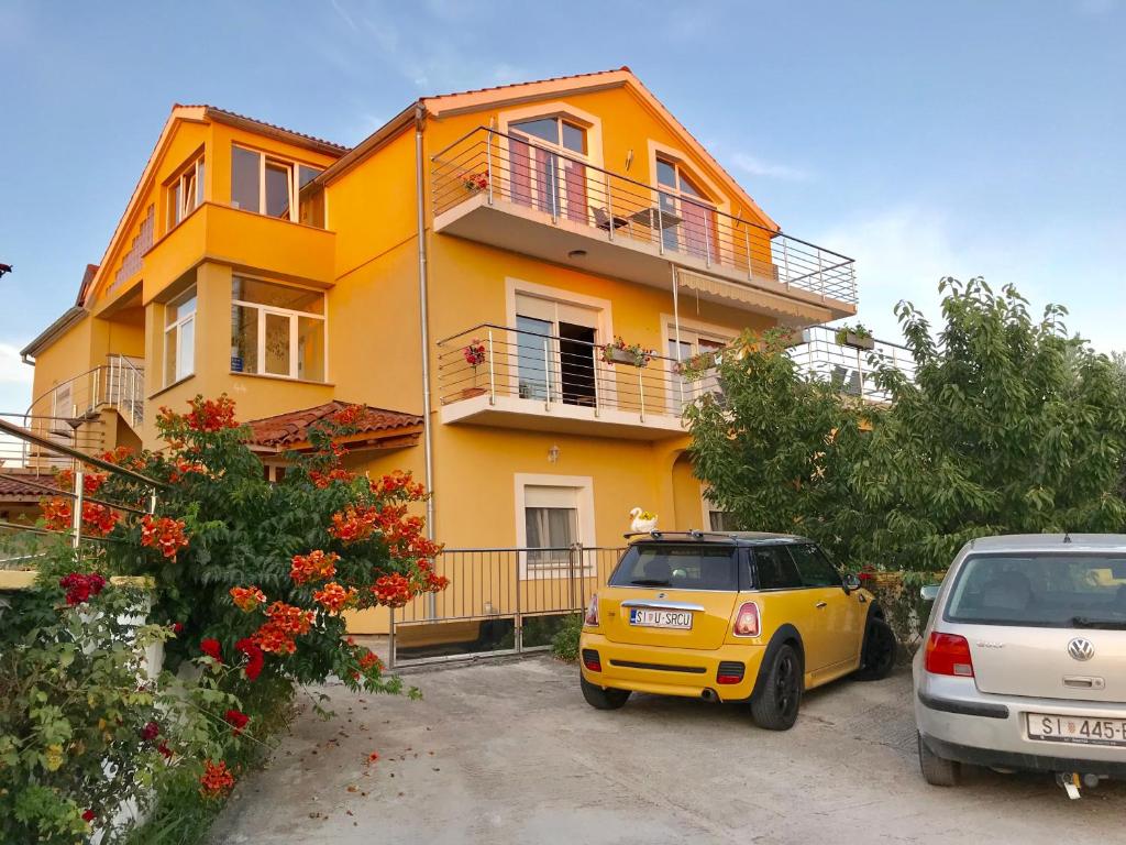a yellow house with cars parked in front of it at Apartments Maslina in Brodarica