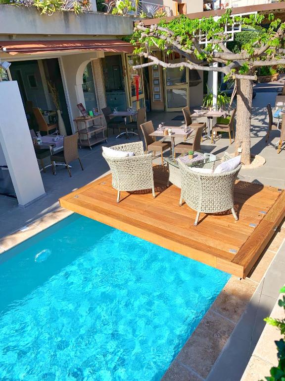 a pool with a wooden deck and chairs and tables at Hôtel Beau Soleil in Le Lavandou