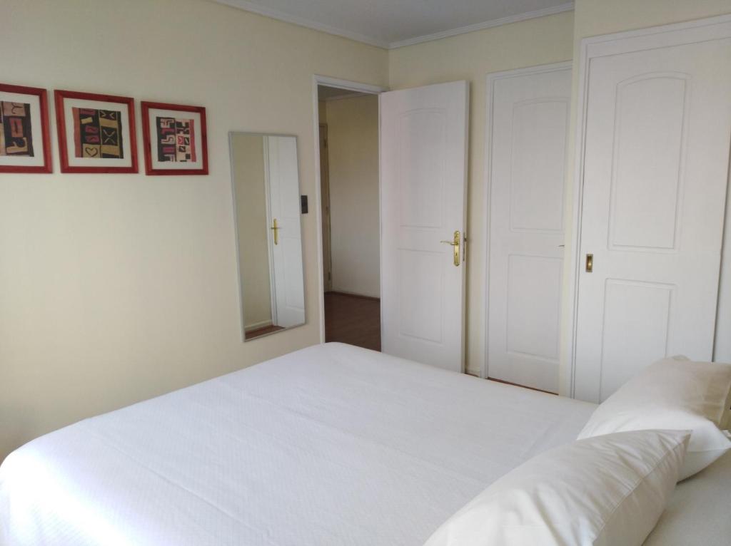 1 dormitorio con cama blanca y espejo en RoomApart Escuela Militar, en Santiago