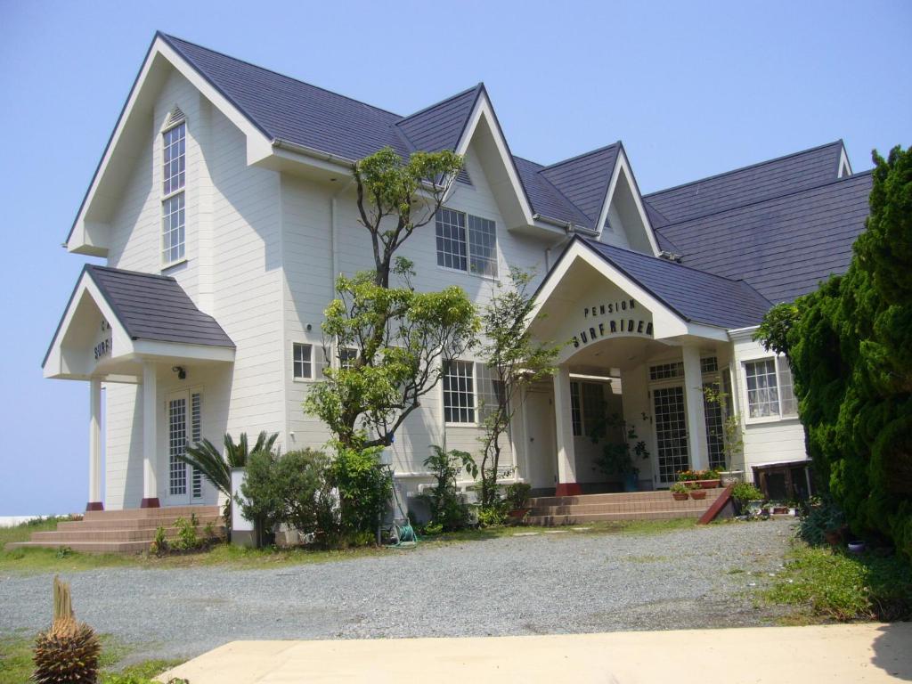 une maison blanche avec un toit noir dans l'établissement Pension Surf Rider, à Nishiizu