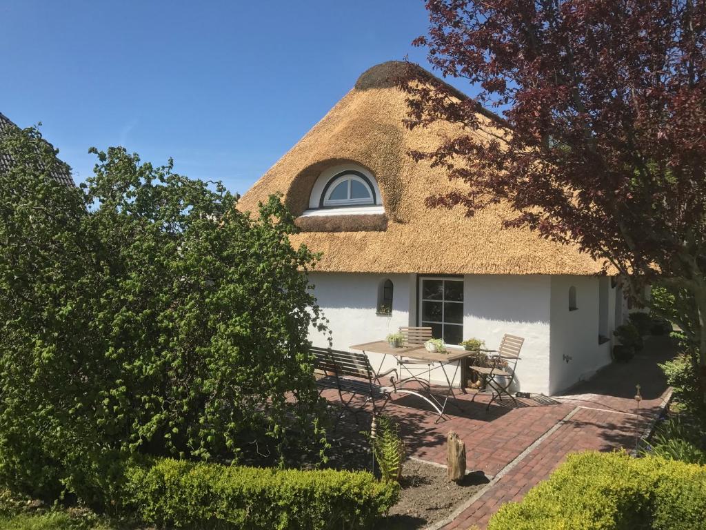 a thatch roofed house with a patio and a window at Refugium im Nordseewind in Norddeich