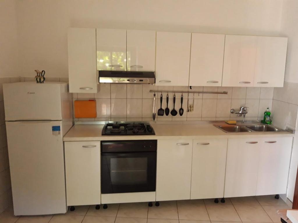 una cucina con armadietti bianchi, piano cottura e frigorifero di Lilo a Maslinica