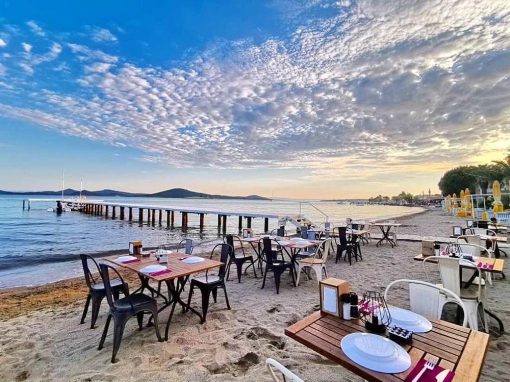 Cunda Hotel في أيفاليك: شاطئ به طاولات وكراسي على الشاطئ