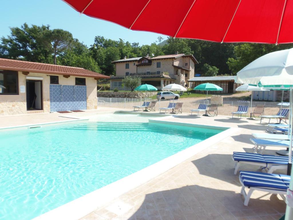 una piscina con ombrellone rosso, sedie e ombrelloni di Aecolibrium Country House a Pastena