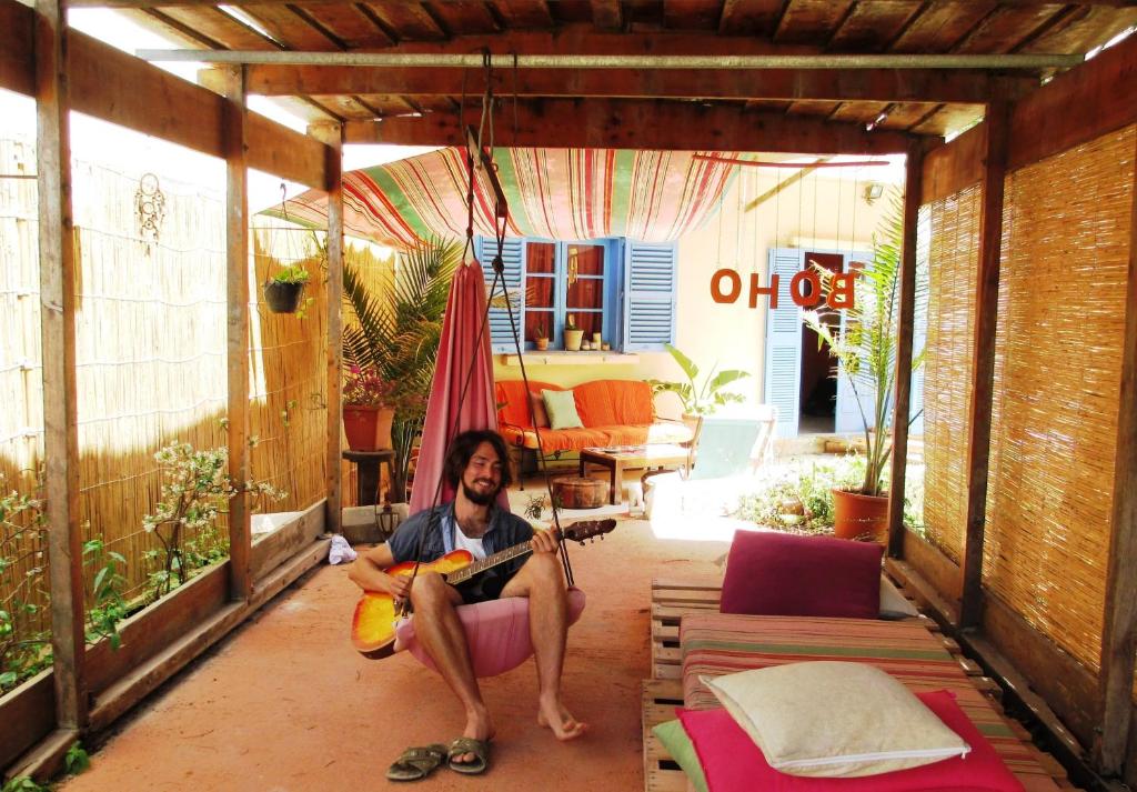 un hombre sentado en una habitación tocando una guitarra en Boho Hostel en San Julián