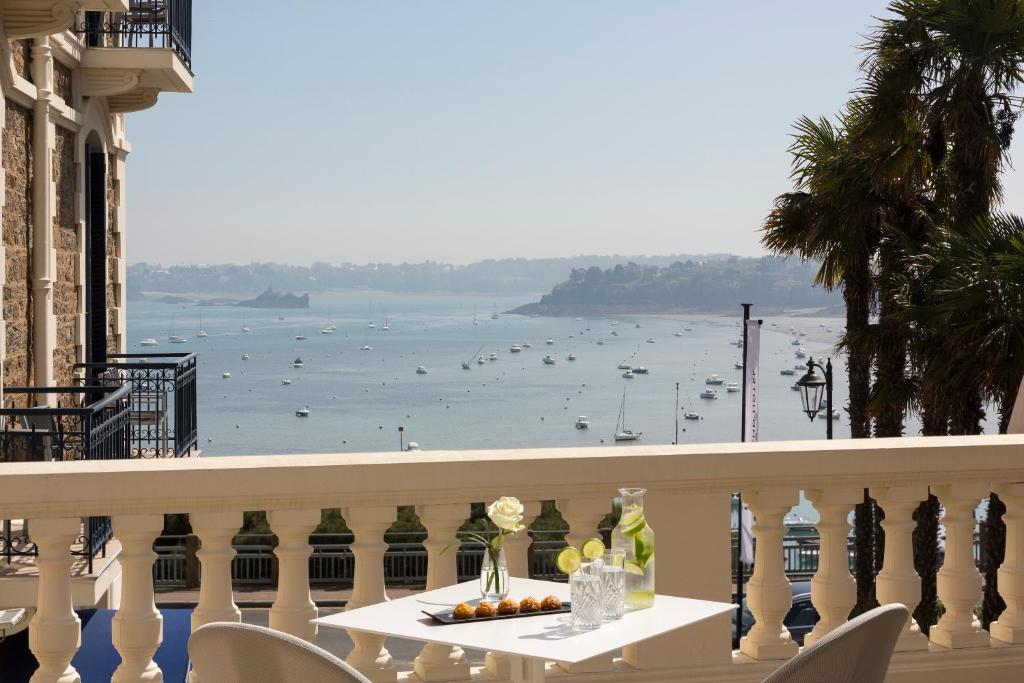 uma varanda com uma mesa e vista para a água em Hôtel Barrière Le Grand Hôtel Dinard em Dinard