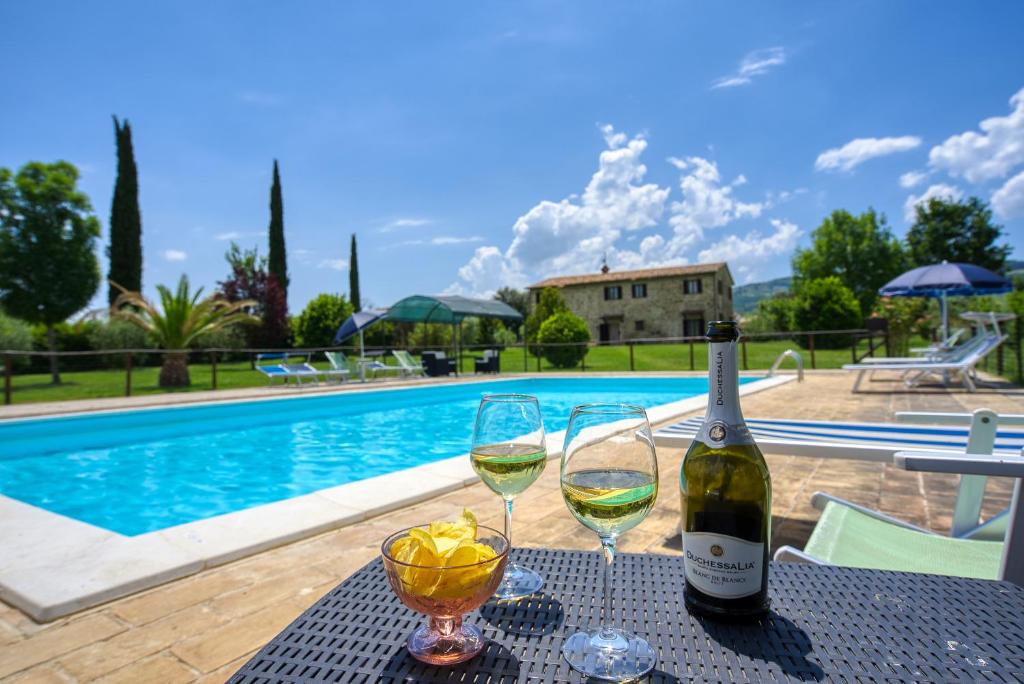 una botella de vino y dos copas en una mesa cerca de una piscina en Agriturismo Le Terre del Casale en Assisi