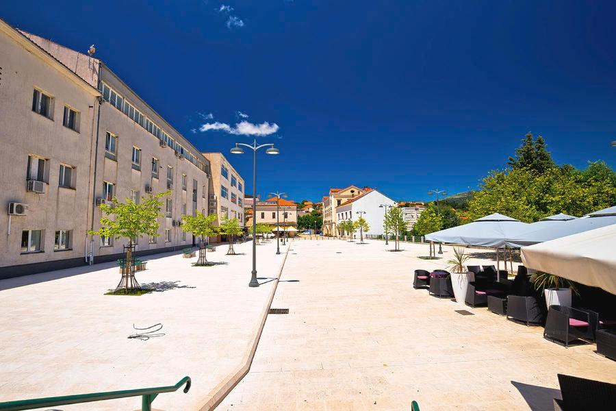 an empty street with tables and umbrellas and buildings at Hotel Park Drniš in Drniš