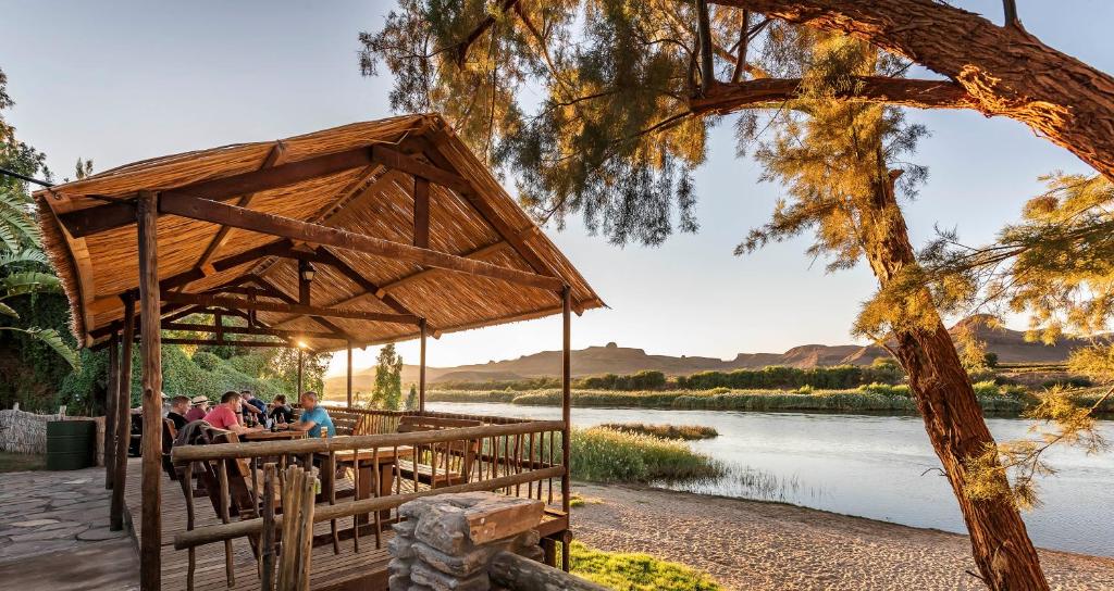 a group of people sitting under a pavilion next to a river at Orange River Rafting Lodge in Kotzeshoop