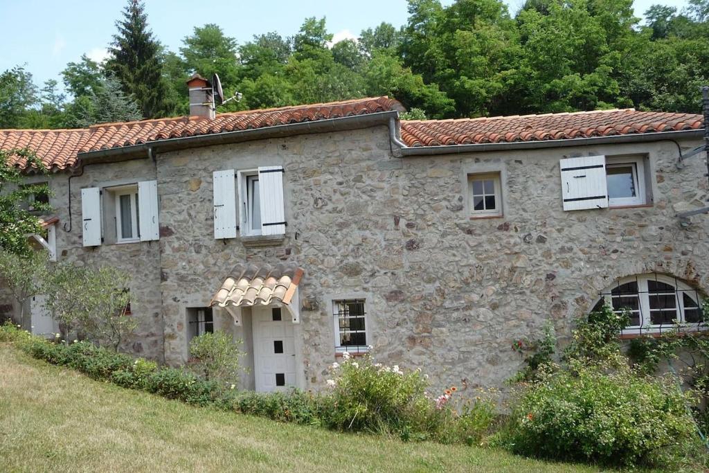 una antigua casa de piedra con ventanas blancas en un campo en maison en pierre dans un écrin de verdure, en Saint-Laurent-de-Cerdans