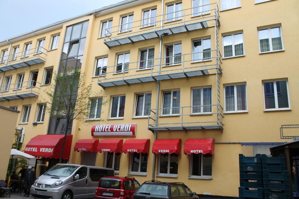 un edificio con toldos rojos y coches aparcados fuera en Hotel Verdi en Múnich