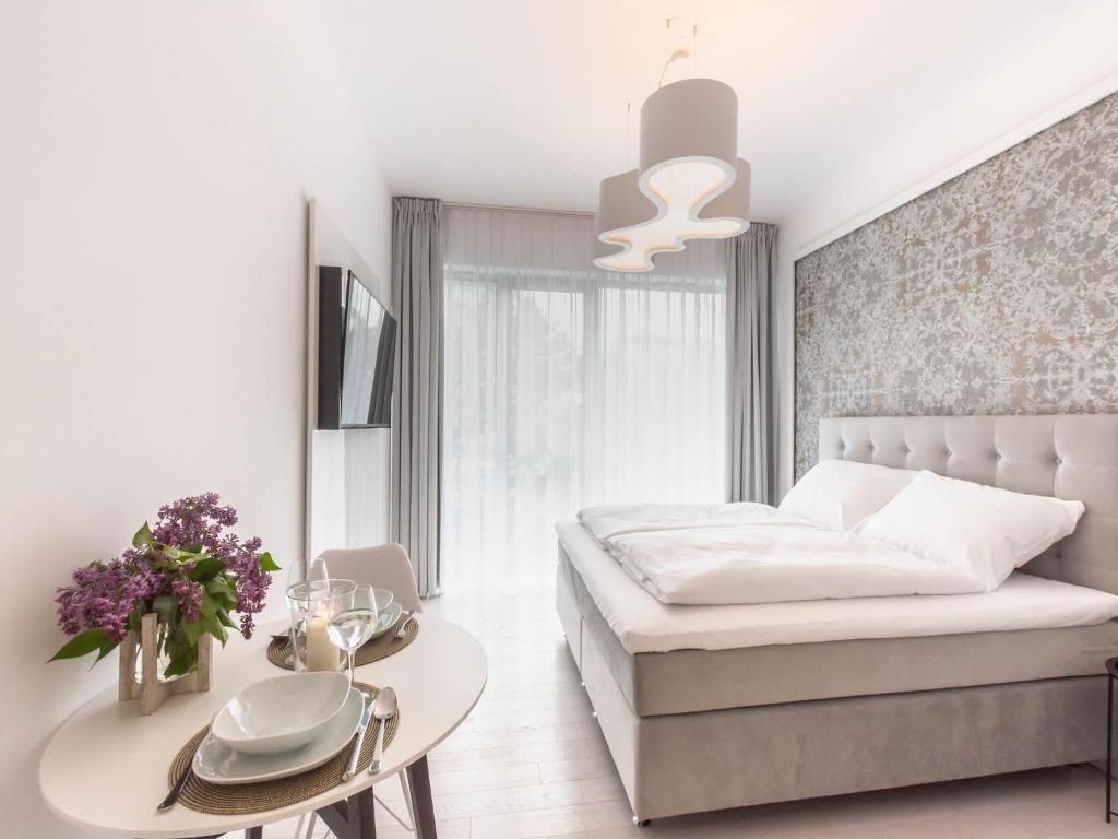 a white bedroom with a bed and a table at VacationClub – Dune B Apartament 3.22 in Mielno