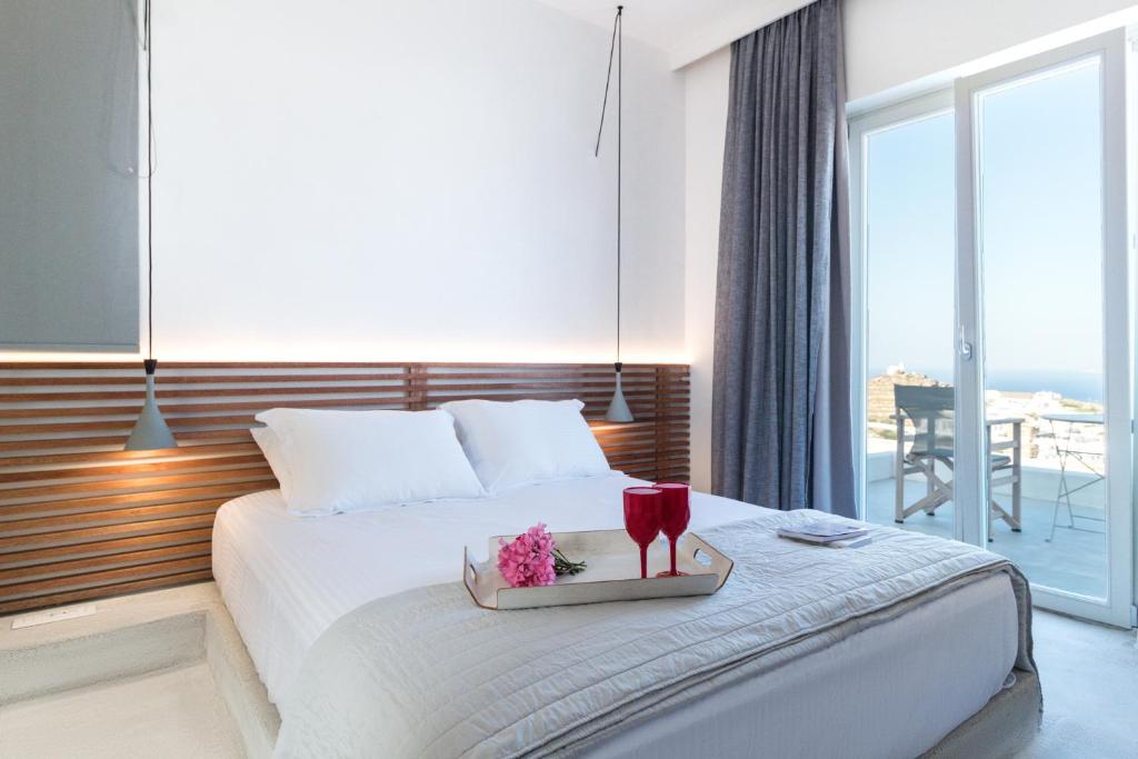 a hotel room with a bed with a tray with two glasses at Wabi Luxury Suites & Maisonettes Ios in Ios Chora