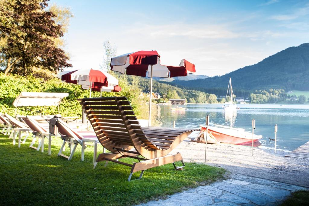 a group of lawn chairs and umbrellas on a beach at Hotel Seewinkel in Fuschl am See