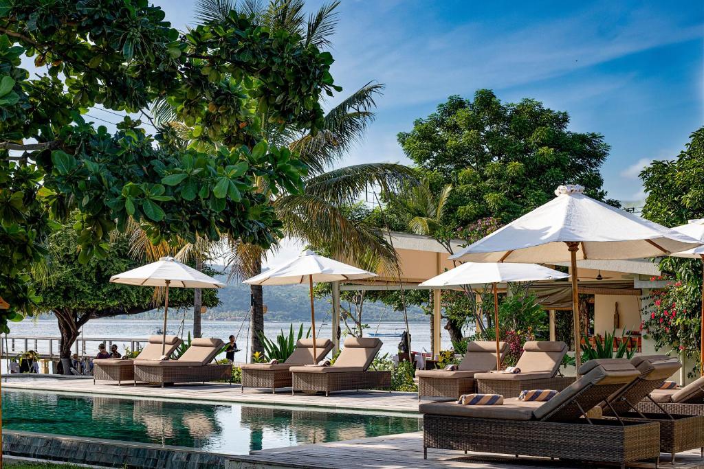 a swimming pool with lounge chairs and umbrellas at Kokomo Resort Gili Gede in Gili Gede