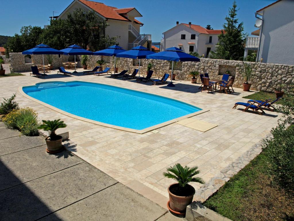 a swimming pool with chairs and blue umbrellas at Apartments Villa Olga in Rab