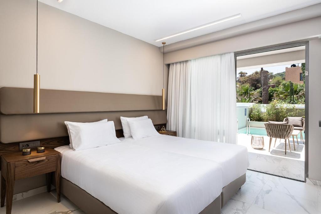 a bedroom with a large white bed and a balcony at Porto Platanias Beach Luxury Selection - Adults Only in Plataniás