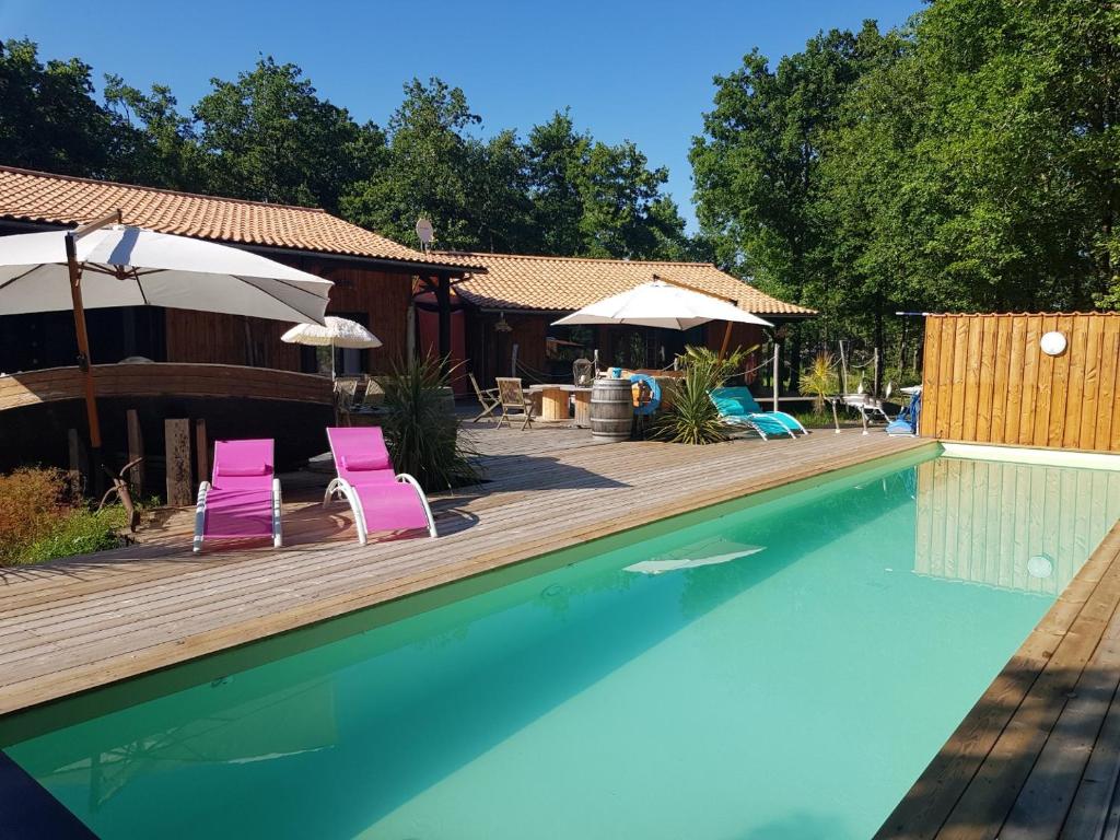 a pool with two pink chairs and a wooden deck at Au Bois Flotté in Hourtin