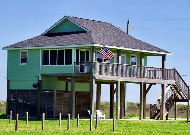 a large green house with an american flag on a porch at Mi Casa Del Mar Home in Caplen