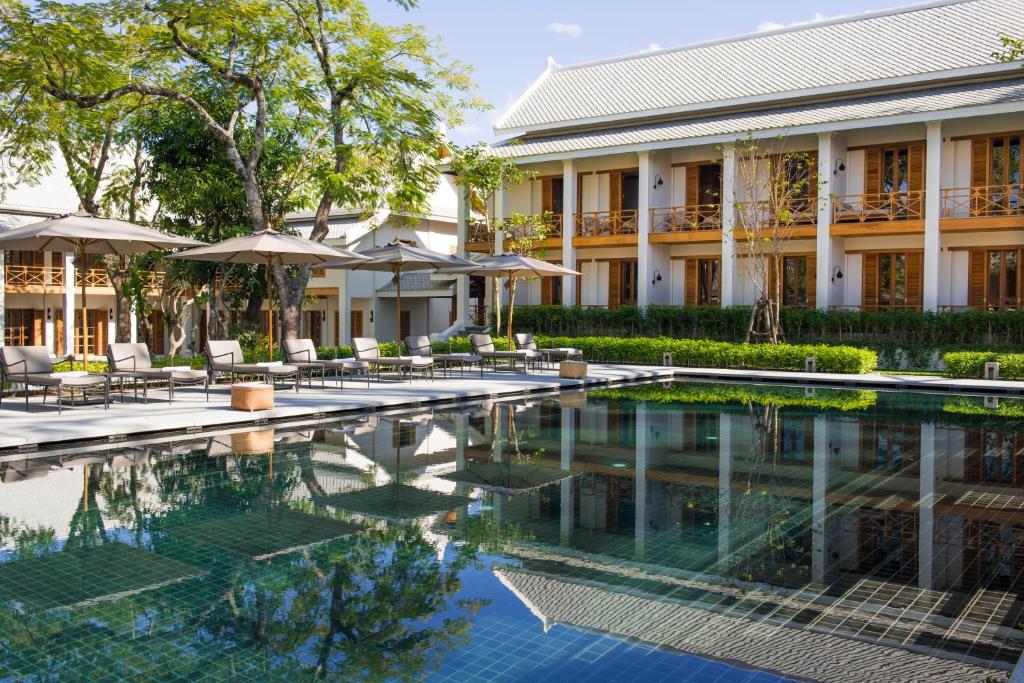 a pool in front of a building with chairs and umbrellas at Avani+ Luang Prabang Hotel in Luang Prabang