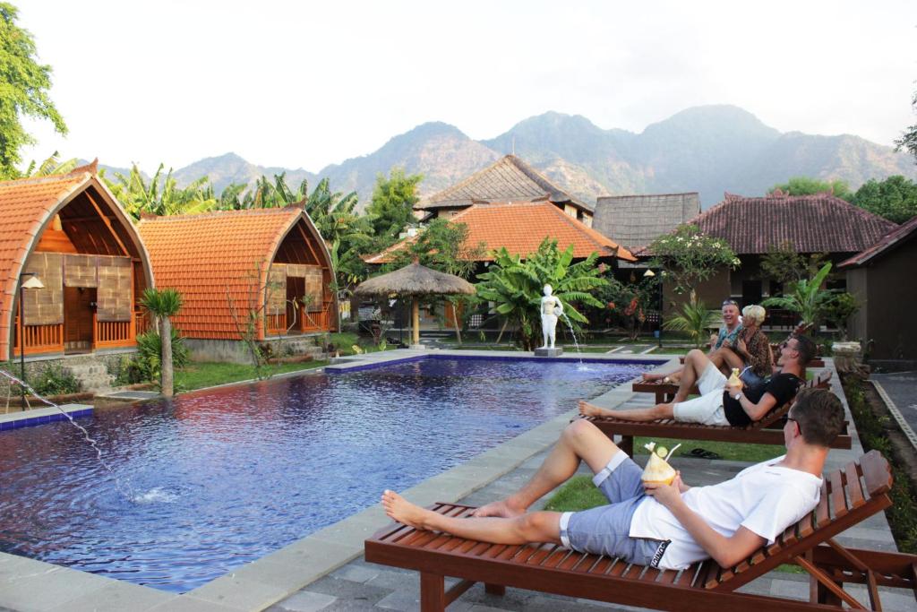 a group of people laying on benches by a swimming pool at Kubu Padi Wooden House in Pemuteran