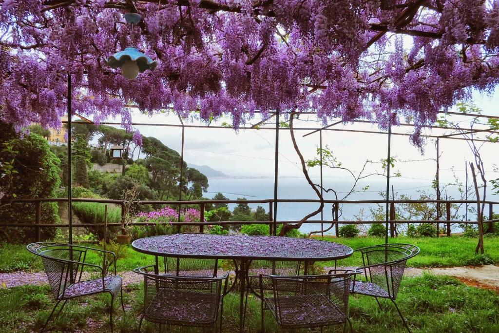 una mesa y sillas con flores púrpuras colgando sobre ella en Villa Maria Antonietta, en Vietri