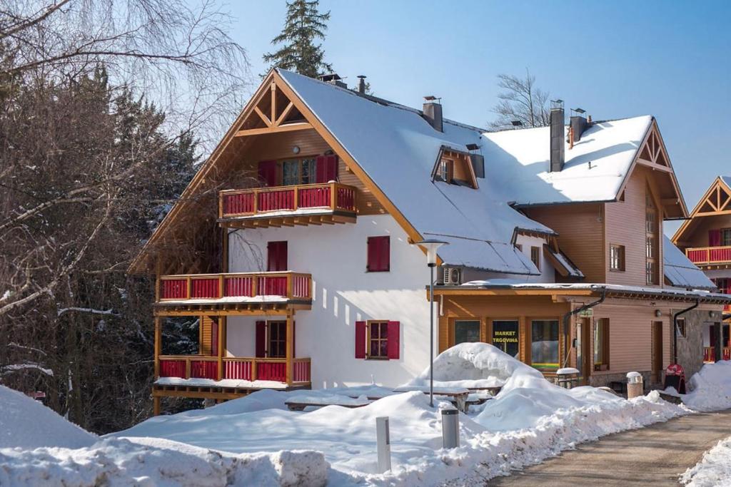a house covered in snow with red windows at Bolfenk lodge apartment in Hočko Pohorje