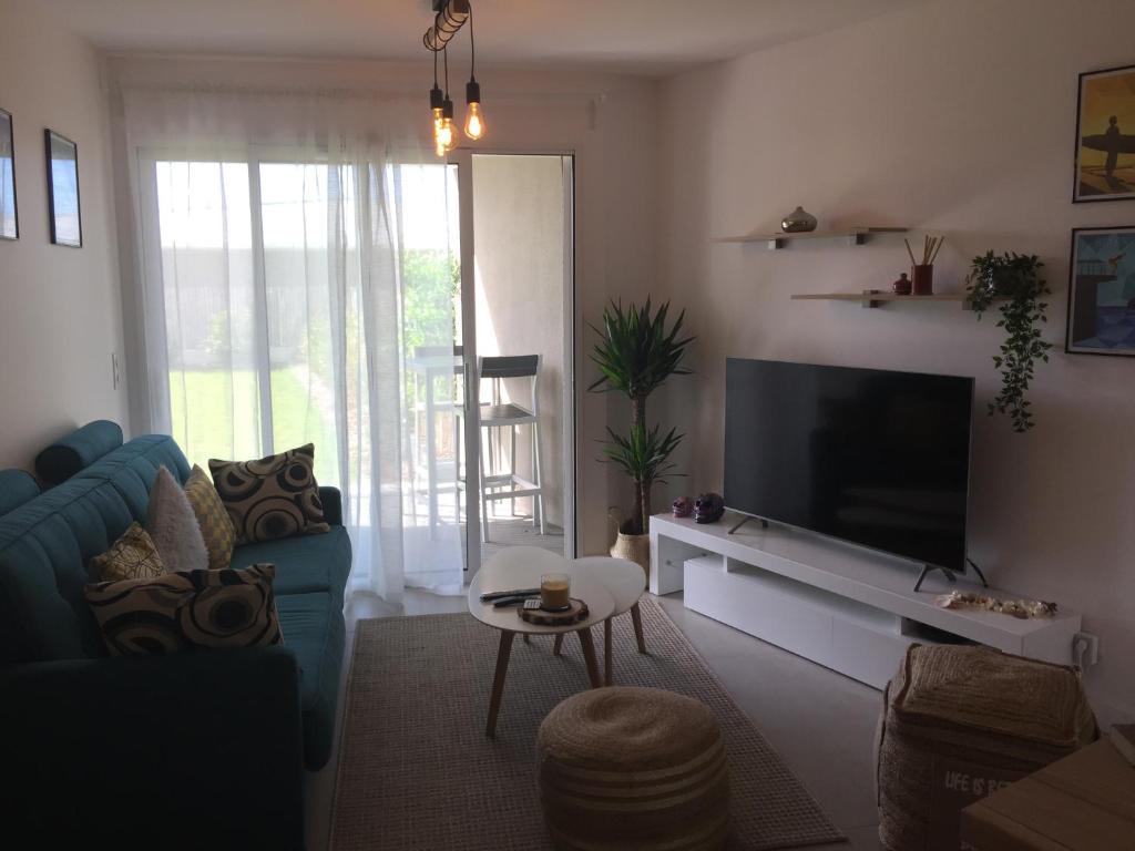 sala de estar con sofá azul y TV de pantalla plana en Anglet Chambre d'Amour, App T2 récent, Classé 4 ét, jardin et parking privé à 100 m des plages, en Anglet