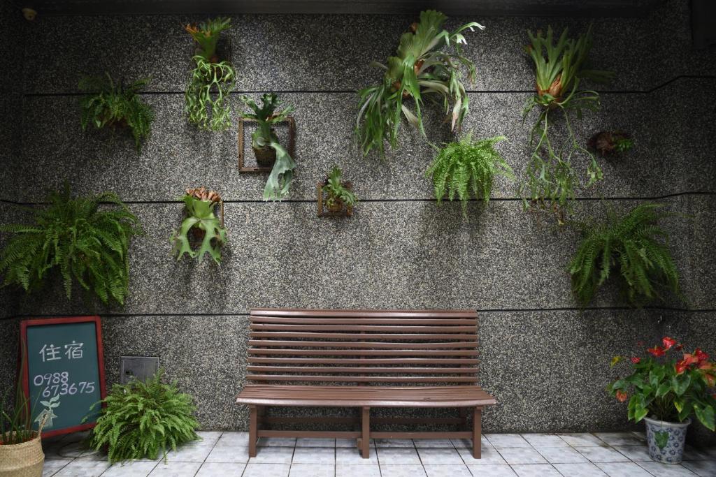 un banco de madera sentado frente a una pared con plantas en Lost and Find Homestay, en Guanshan