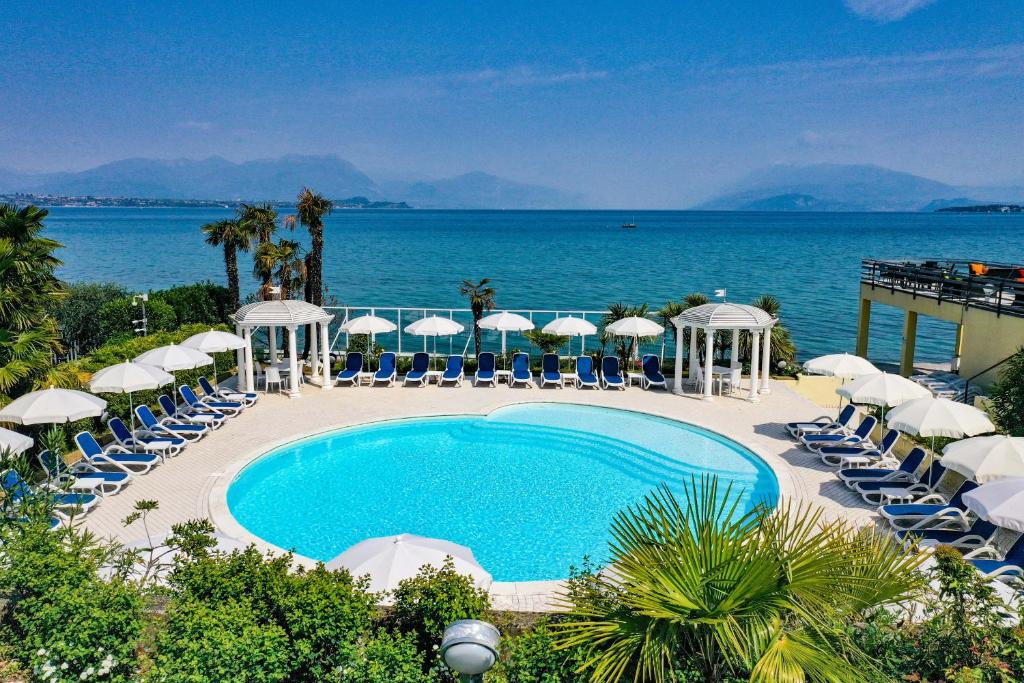 einen Pool mit Stühlen und Sonnenschirmen sowie das Meer in der Unterkunft Lido International in Desenzano del Garda