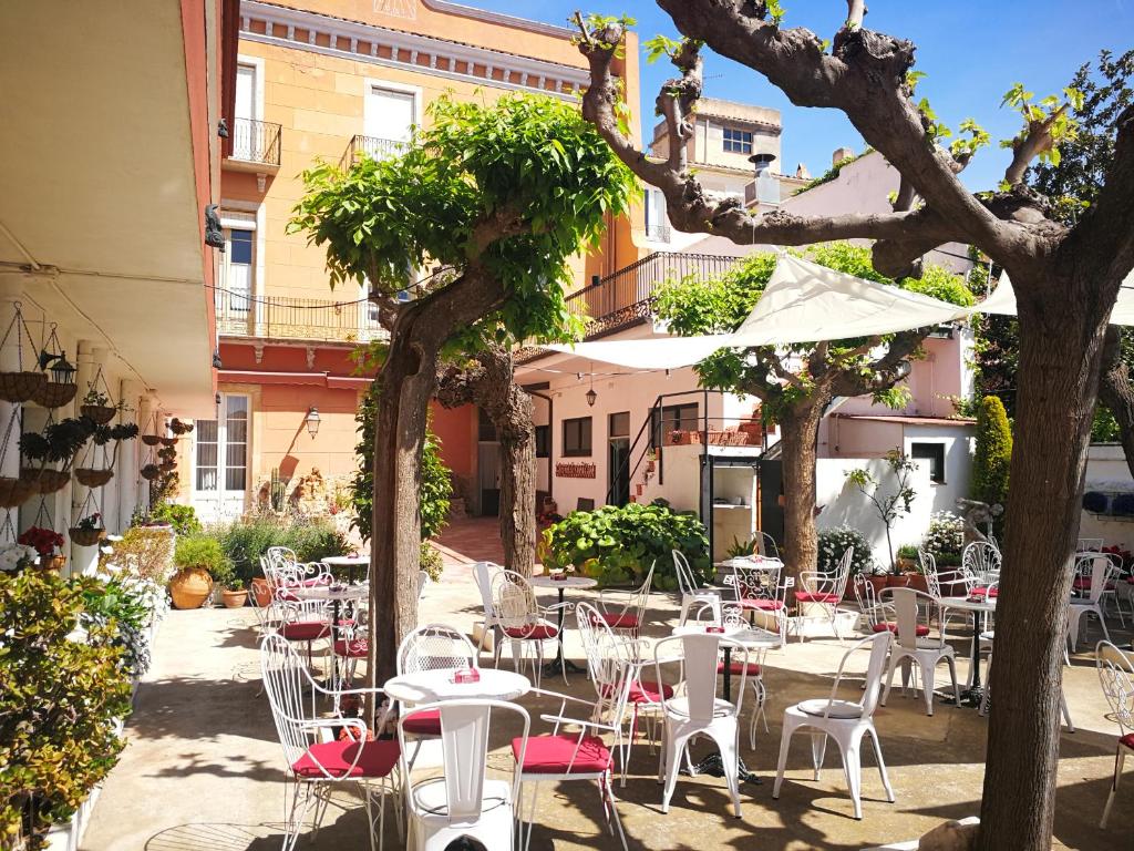 un patio con mesas blancas, sillas y árboles en Hostal Plaja i Pati de Can Plaja, en Palafrugell