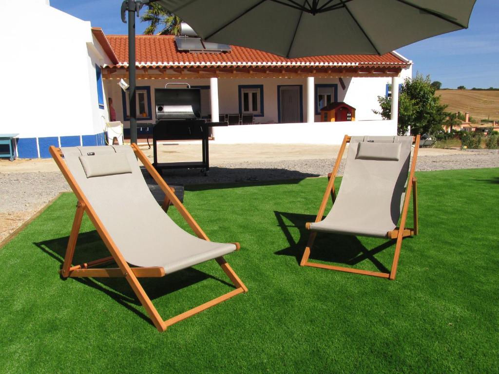 two lawn chairs sitting on the grass under an umbrella at Casa do Chaparral campo e praia in Cercal